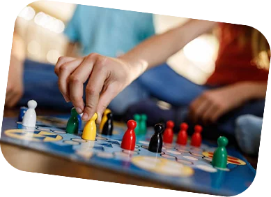 Primo piano della mano di un giocatore che sposta una pedina gialla su un tabellone da gioco colorato insieme ad altre pedine.