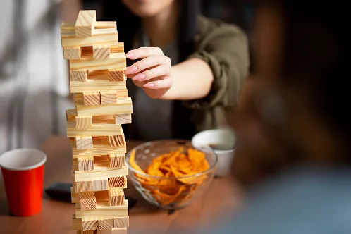 Primo piano della mano di una persona che estrae con cura un blocco di legno da una torre traballante durante un gioco da tavolo.